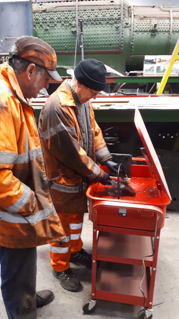 Keith looks on as John Dixon cleans FR 20's tender axlebox lids in the new cleaning tankhe