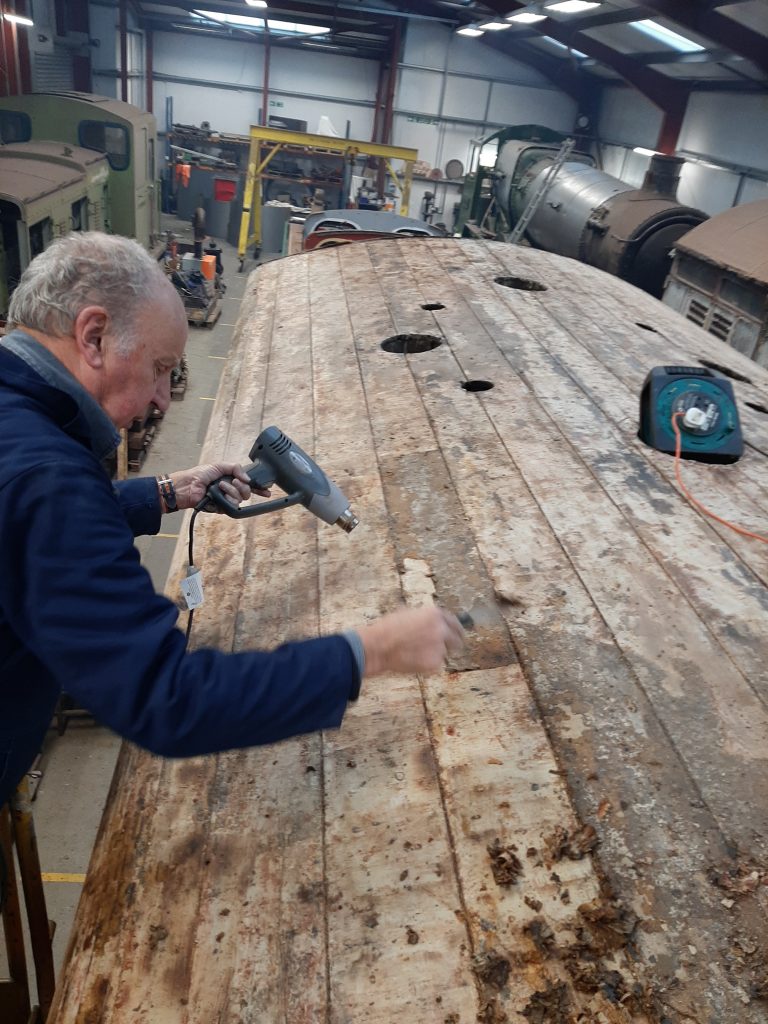 Phil Burton scraping away the old canvas bonding compound . Progress can clearly be seen.