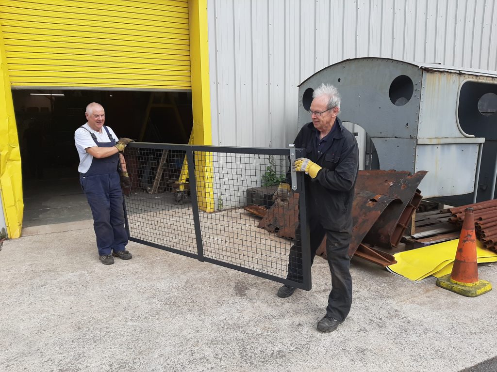 John Davis and John Dixon move the door of the gas cylinder cage into position