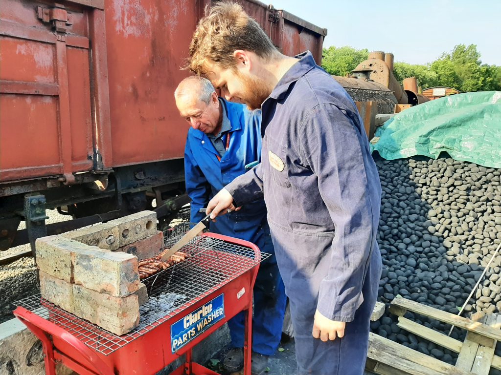 Jack Davenport and Peter Liddle cook sausages on the 'new' barbeque, converted from a scrap parts washer.